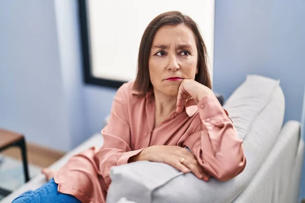 Middle age woman with sad expression sitting on sofa at home