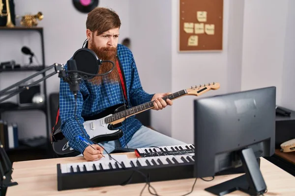 Young redhead man musician composing song playing electrical guitar at music studio