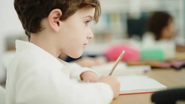 Adorable caucasian boy student writing on notebook studying at classroom