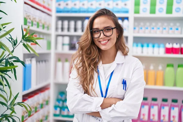 Young beautiful hispanic woman pharmacist smiling confident standing with arms crossed gesture at pharmacy