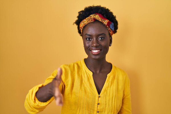 African young woman wearing african turban smiling friendly offering handshake as greeting and welcoming. successful business.