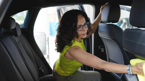 Middle age hispanic woman cleaning car interior with microfiber cloth at car wash station