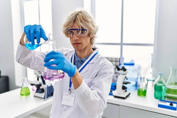 Young blond man scientist pouring liquid on test tube at laboratory