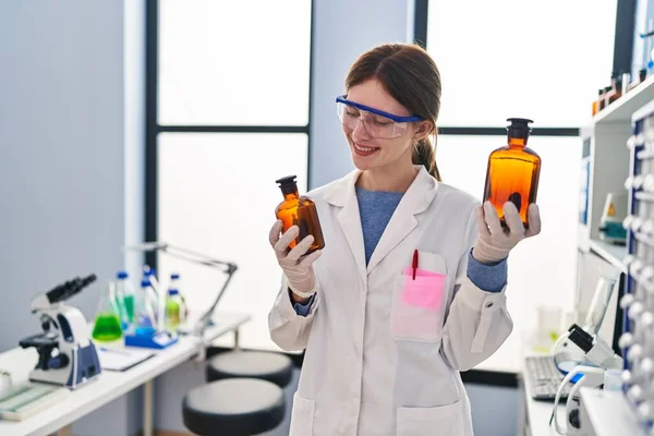 Giovane Scienziata Bionda Che Tiene Bottiglie Con Liquido Sorridente Laboratorio — Foto Stock