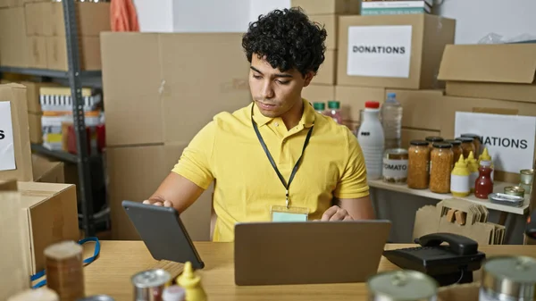 年轻的拉丁男子志愿使用笔记本电脑和触摸板坐在慈善中心的桌子上 — 图库照片