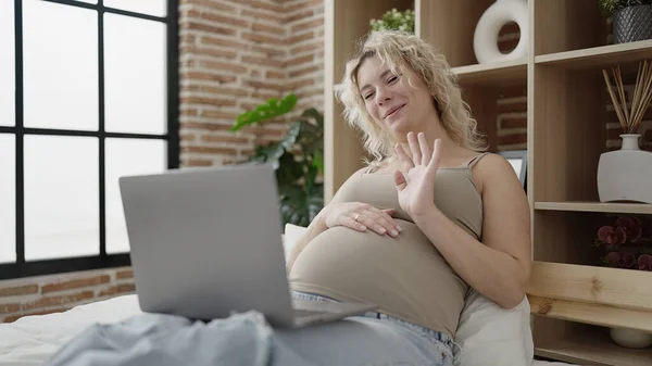 年轻的孕妇在卧室里有电视呼叫触摸腹部 — 图库照片