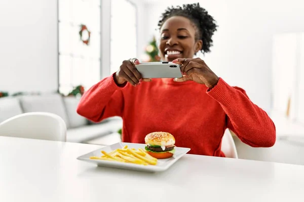 Afričanky Americká Žena Fotit Smartphone Hamburger Sedí Stole Vánočního Stromku — Stock fotografie