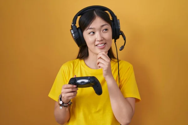 中国年轻女子手牵着下巴玩电子游戏控制器 思考问题 沉思的表情 微笑和体贴的脸 怀疑概念 — 图库照片