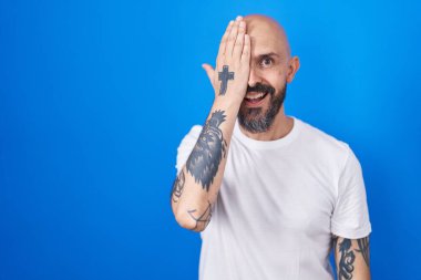 Mavi arka planda duran İspanyol dövmeli adam bir gözünü eliyle kapatıyor, yüzünde kendine güvenen bir gülümseme ve sürpriz bir duygu var.. 