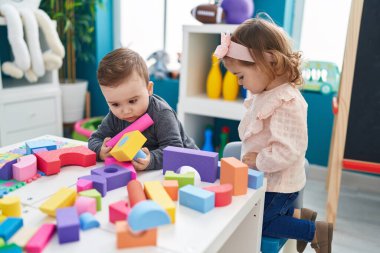 Anaokulundaki masada oturan sevimli kız ve oğlan inşaat bloklarıyla oynuyorlar.