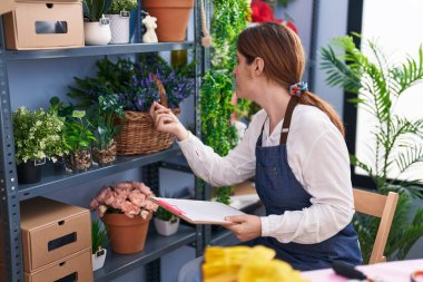 Çiçekçide doküman okuyan genç bir kadın.