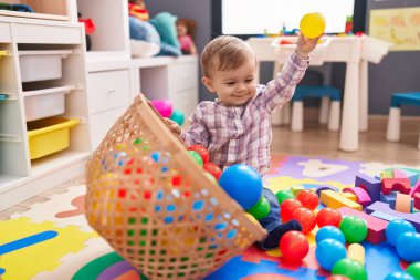 Anaokulunda yerde taşaklarıyla oynayan sevimli beyaz çocuk.