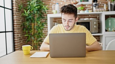 Genç İspanyol öğrenci yemek odasındaki masada dizüstü bilgisayar kullanıyor.