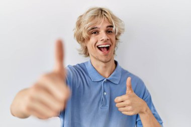 İzole edilmiş arka planda duran genç modern adam elleriyle olumlu bir jest yapmayı onaylıyor, gülümsüyor ve başarı için seviniyor. kazanan jest. 