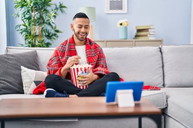 Genç İspanyol adam patlamış mısır yiyor tablet cihazından film izliyor ve kahkahalarla gülüyor.. 