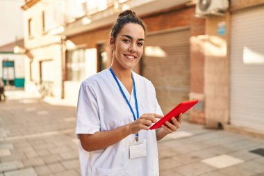 Young beautiful hispanic woman physiotherapist smiling confident using touchpad at street