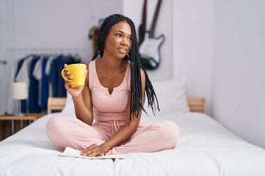 Afrikalı Amerikalı kadın yatak odasında bir fincan kahve içip gazete okuyor.