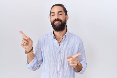 Sakallı, sıradan tişörtlü, kendine güvenen, parmakları farklı yönleri gösteren İspanyol bir adam. reklam için kopyalama alanı 