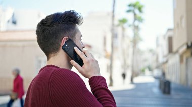 Young hispanic man talking on smartphone with serious expression at street