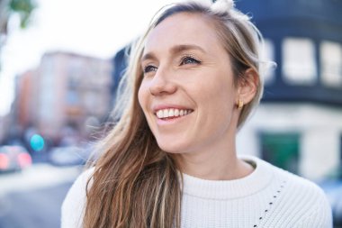 Young blonde woman smiling confident looking to the side at street