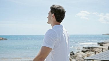 Genç İspanyol adam kumsalda kolları açık nefes alıyor.