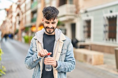 Genç İspanyol adam gülümsüyor. Elinde bir şişe su tutuyor.