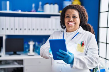 African american woman scientist smiling confident using touchpad at laboratory