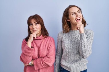 Anne ve kızı mavi arka planda el pençe divan durup soru sormayı, düşünceli ifadeyi düşünüyorlar. Gülümseyen ve düşünceli bir yüz. şüphe kavramı. 