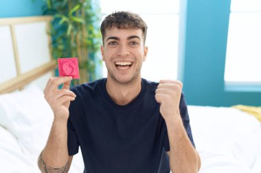 Genç İspanyol adam yatakta oturmuş elinde prezervatif tutarak gururla bağırıyor zaferi ve başarıyı kutluyor. Kollarını kaldırıp heyecanla bekliyor. 