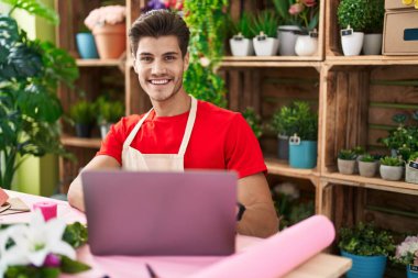 Young hispanic man florist smiling confident using laptop at flower shop
