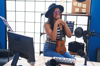 Müzik stüdyosunda ukulele tutarak gülümseyen Afrikalı Amerikalı kadın müzisyen.