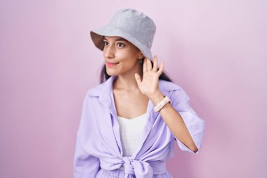 Pembe arka planda dikilen, şapkalı, ağzı kulaklarına varan bir gülümsemeyle dedikodu ya da dedikoduları dinleyen genç İspanyol kadın. Sağırlık kavramı. 