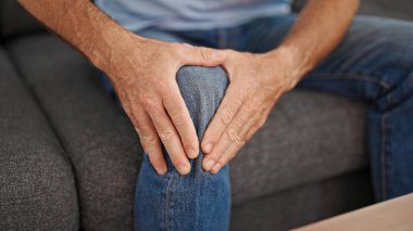 Orta yaşlı bir adam evinde dizinden sakatlanarak koltukta oturuyor.