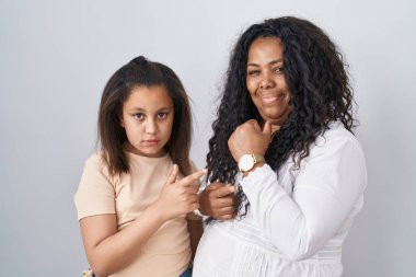 Anne ve küçük kızı beyaz arka planda aceleyle dikiliyorlar. Saati, sabırsızlığı ve rahat bir ifadeyle kameraya bakıyorlar. 