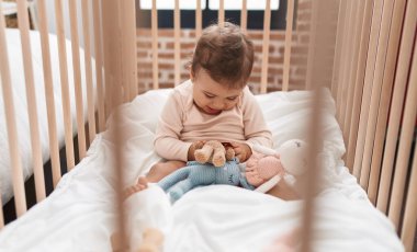 Sevimli İspanyol bebek beşikte oturuyor ve yatak odasında oyuncaklarla oynuyor.