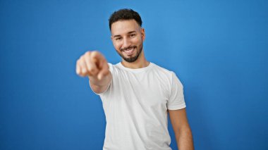 Genç Arap adam, izole edilmiş mavi arka planda kameraya işaret eden birini arıyor.