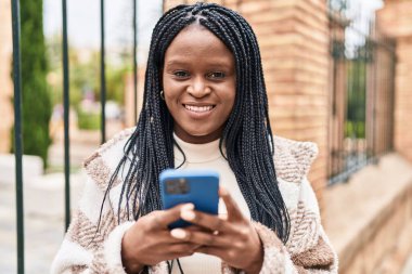 Afro-Amerikalı kadın sokakta akıllı telefon kullanarak kendine güveniyor.