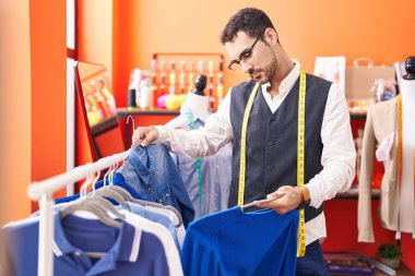 Genç İspanyol terzi atölyedeki askıda giysileri tutuyor.