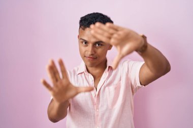 Pembe arka planda duran genç İspanyol adam el ve parmakları kullanarak çerçeve yapıyor, kamera bakış açısı. 