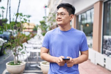 Young chinese man smiling confident using smartphone at coffee shop terrace