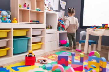 Adorable hispanic girl standing on back view at kindergarten