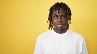 İzole edilmiş sarı arka plan üzerinde ciddi bir ifadeyle duran Afrikalı Amerikalı adam.