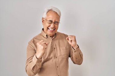 İspanyol kıdemli gözlüklü çok mutlu ve heyecanlı bir jest yapıyor. Kolları havada, gülümsüyor ve başarı için bağırıyor. kutlama konsepti. 