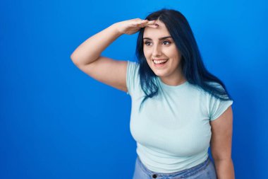 Mavi arka planda duran mavi saçlı, mutlu ve gülümseyen genç, modern bir kız. arama kavramı. 