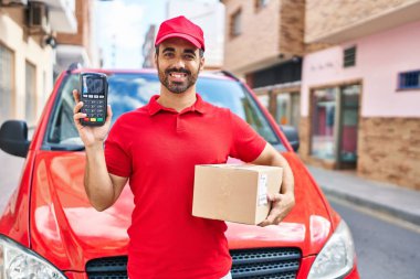 Sakallı, teslimat üniforması giyen ve elinde veri bankası olan mutlu ve havalı bir gülümsemeyle gülümseyen genç bir İspanyol. diş gösterme. 