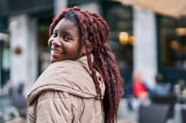 Afro-Amerikalı kadın kahvecinin terasında kendine güvenerek gülümsüyor.