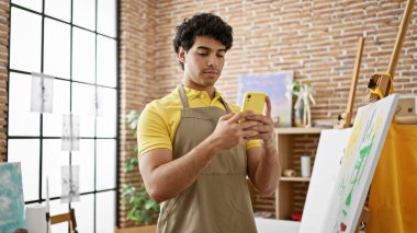 Sanat stüdyosunda akıllı telefon kullanan genç Latin bir sanatçı.
