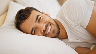 Genç İspanyol adam yatakta kendinden emin bir şekilde gülümsüyor.