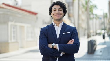 Young latin man business worker smiling confident standing with arms crossed gesture at street