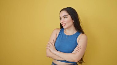 Kolları çapraz hareketlerle duran genç, güzel İspanyol kadın. Evet diyor. İzole edilmiş sarı arka planda.